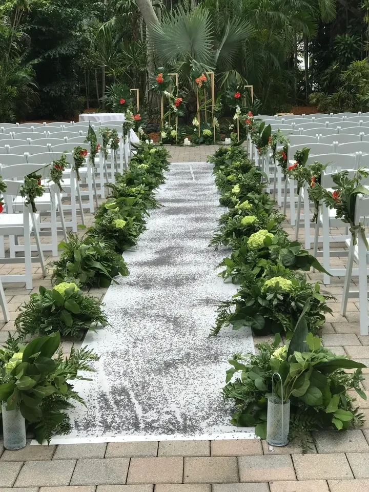Outdoor ceremony aisle with lush green botanical decor and sequin runner