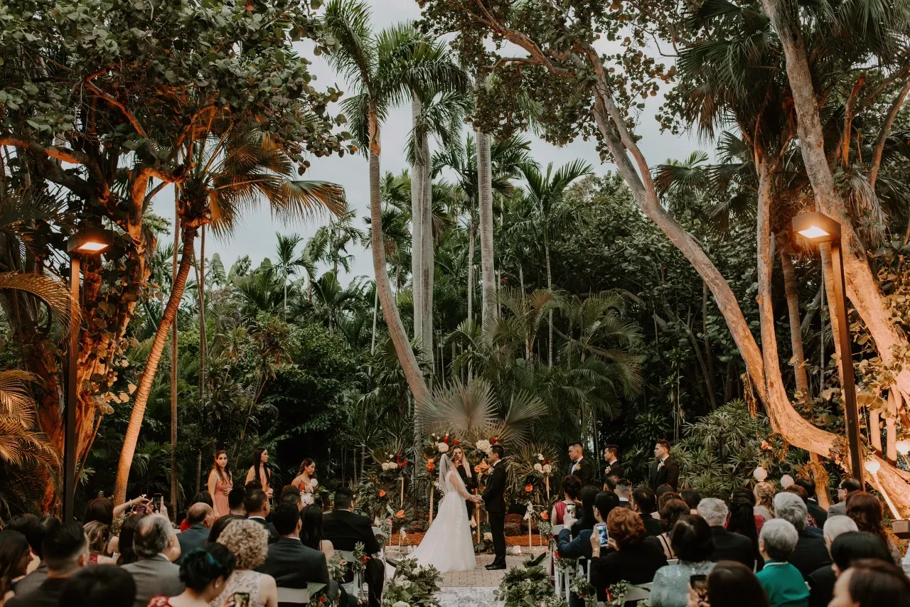 Outdoor tropical garden wedding ceremony at dusk with full audience