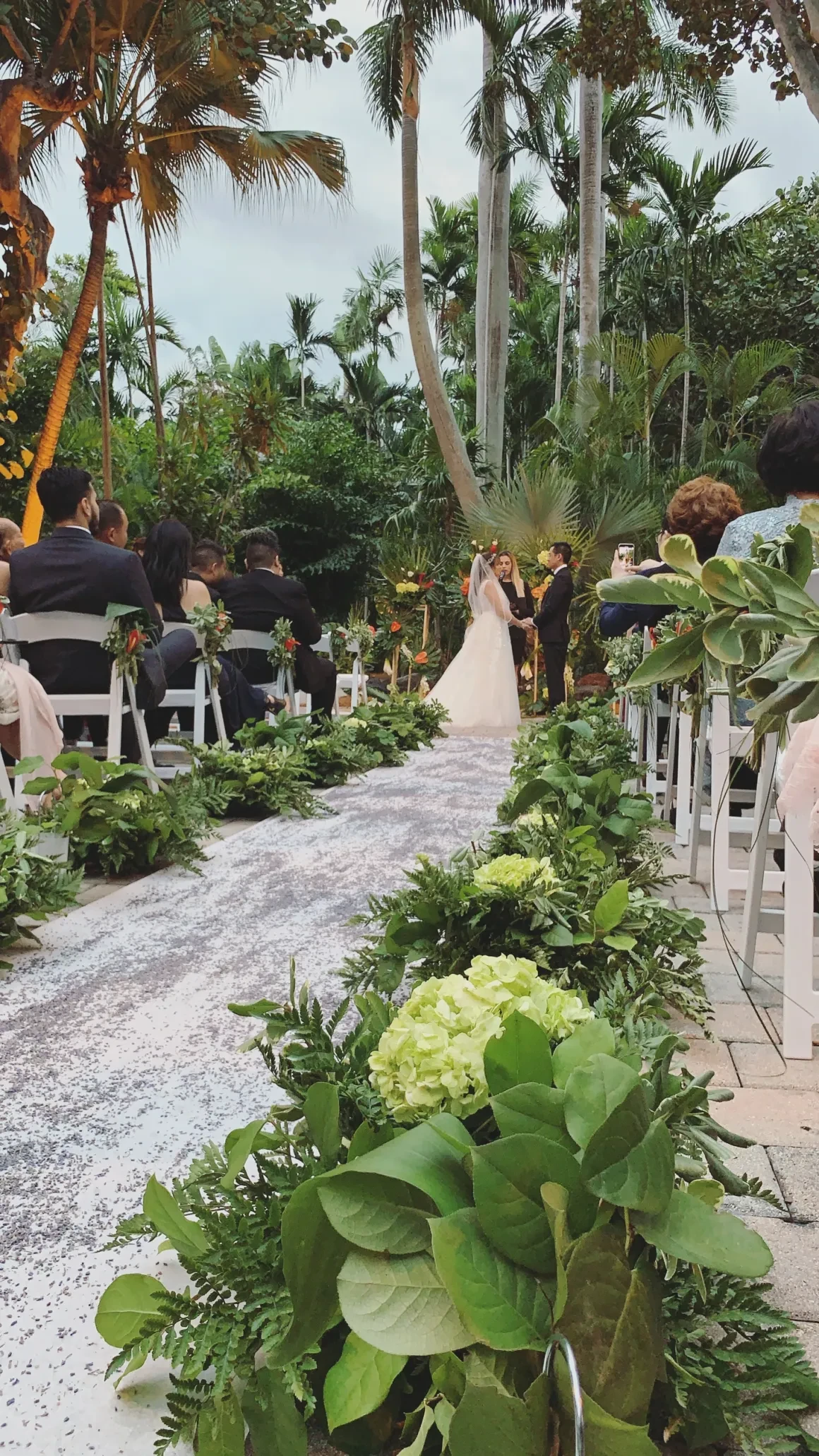 Tropical garden wedding ceremony with palm trees and white chairs