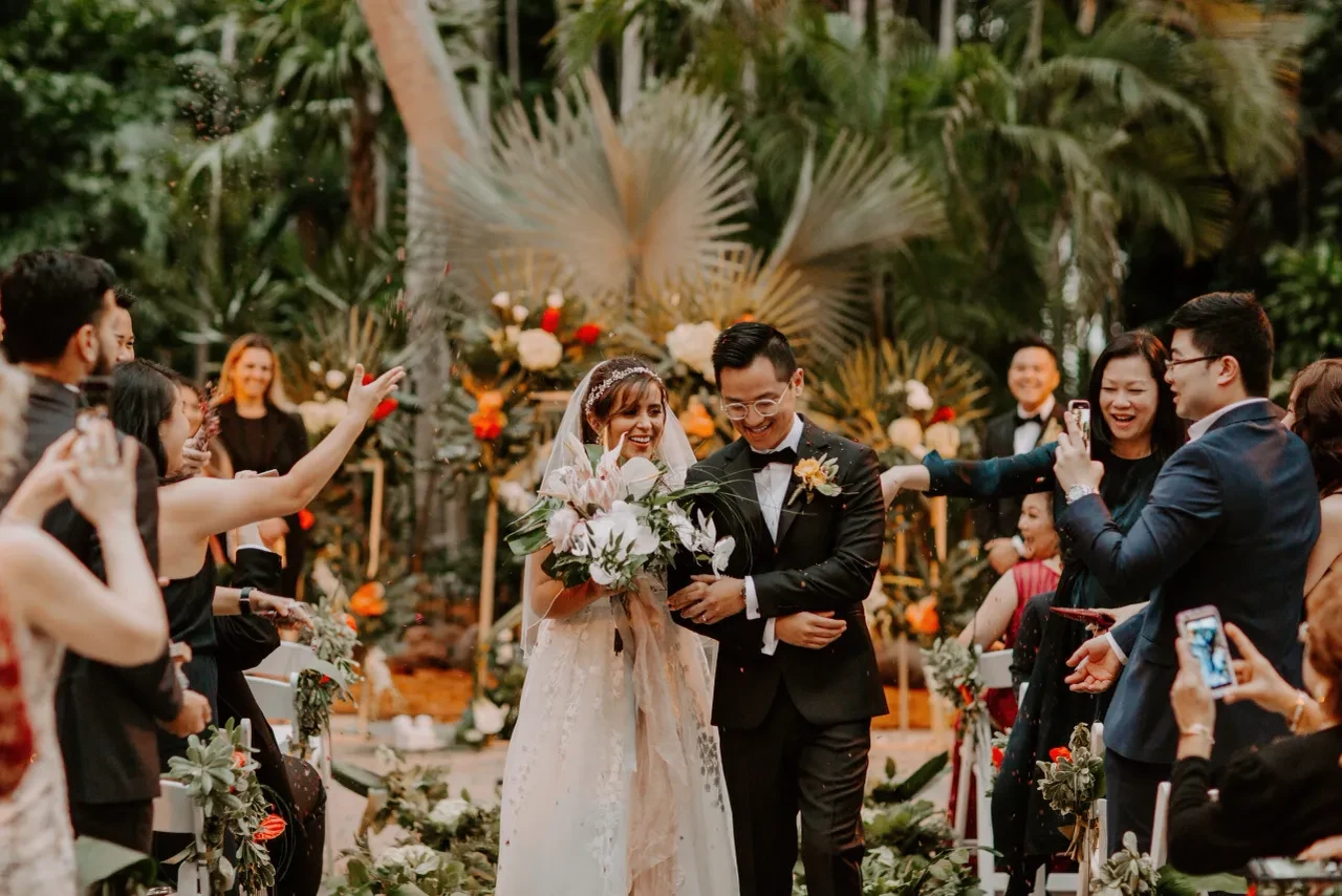 Bride and groom walking down the aisle with confetti and tropical florals
