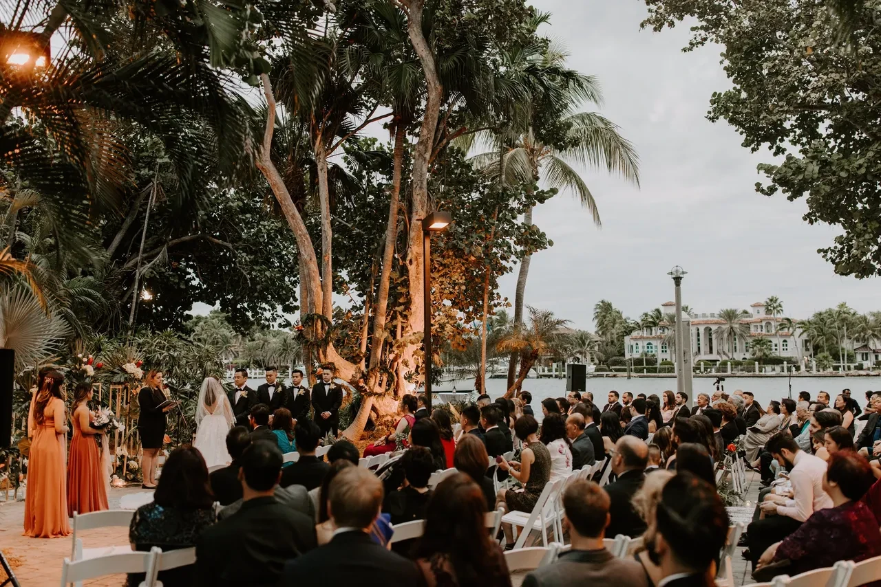 Wedding ceremony by the waterfront with tropical trees at sunset
